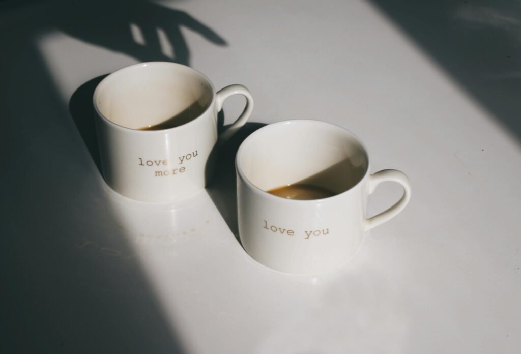 Pair of ceramic mugs with 'love you' text, casting artistic shadows on a white surface.