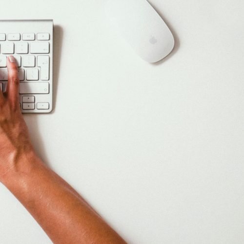 Close-up of hands typing on a keyboard with a yellow watch on the desk
